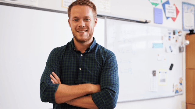 Male Teacher smiling in Front of Whiteboard in Classroom
